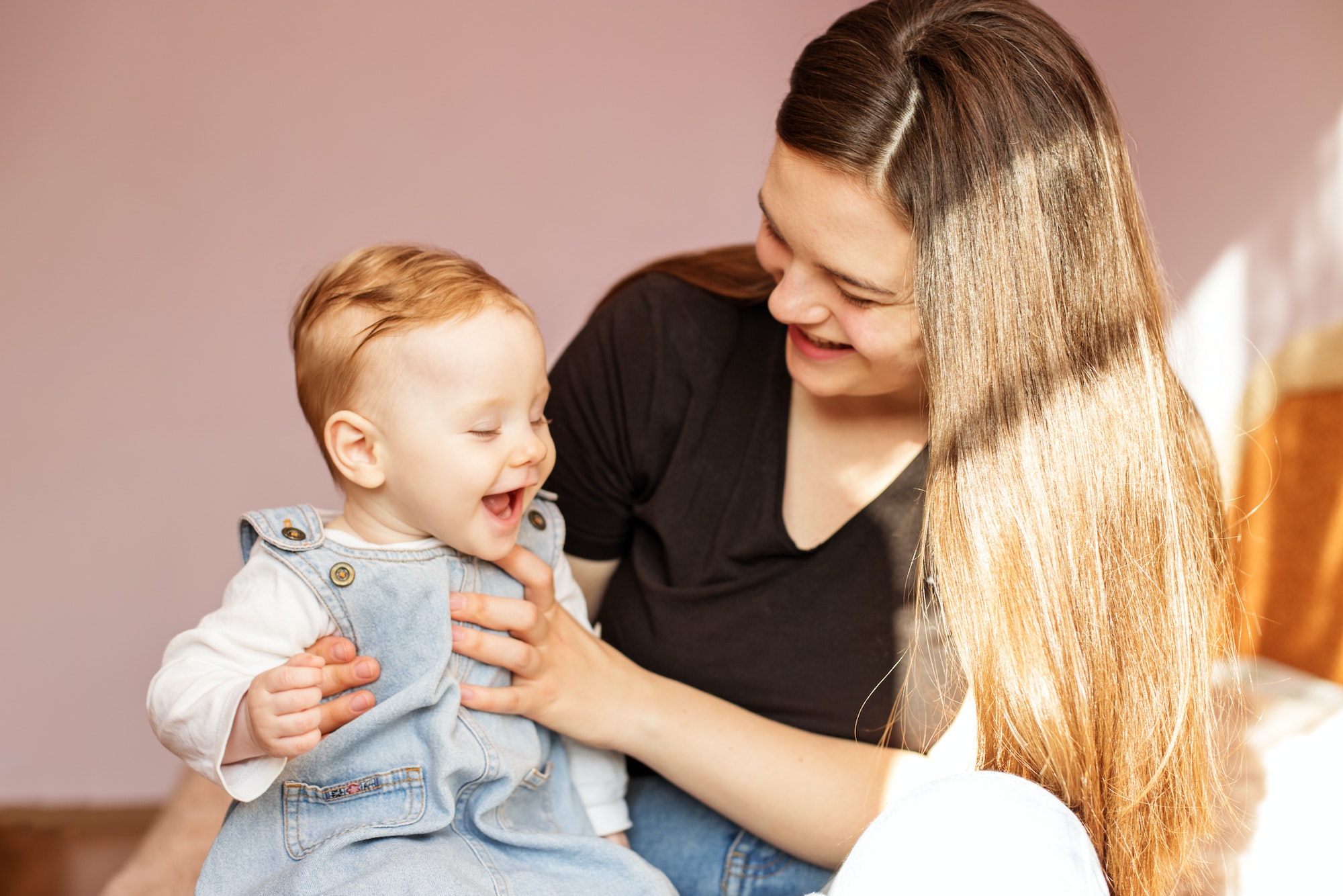 Happy mom holds little daughter on lap. Mother and little todler girl are playing in room.